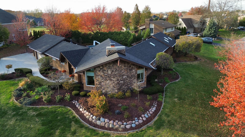 Aerial view of stone-front home with new architectural shingle roof, fall foliage