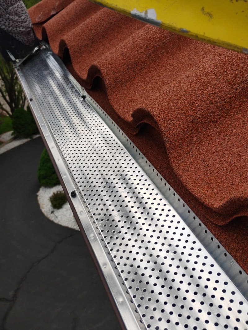 Perforated aluminum gutter guard installed over a seamless gutter on a stone-coated metal tile roof