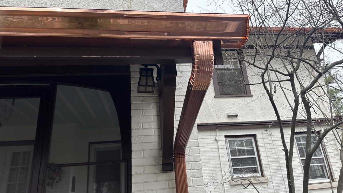 Custom copper K-style gutters and a crimped copper downspout installed along the eave of a brick and stucco home