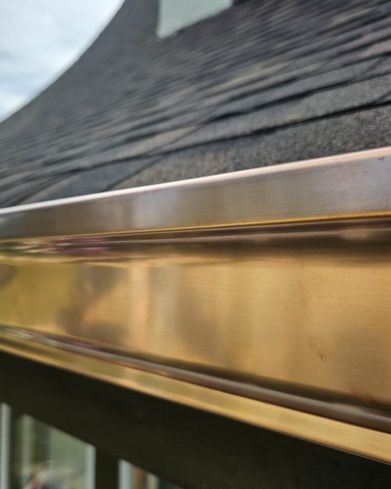 Custom copper box gutter along a shingle roof eave, polished copper not yet patinated