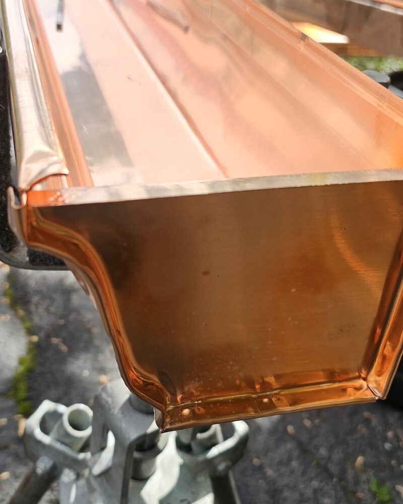 Copper K-style gutter being custom fabricated on site, showing the soldered end cap and ogee profile