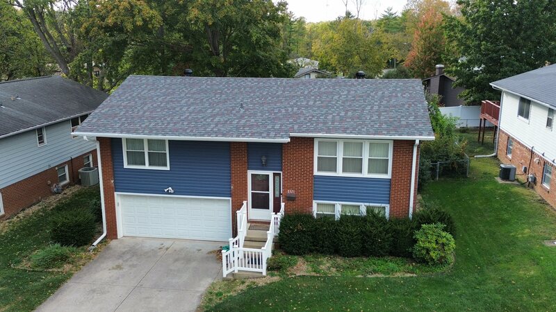 The same Decatur IL raised ranch after siding replacement, new blue horizontal lap siding on the gables and over the garage with white window trim, red brick body retained