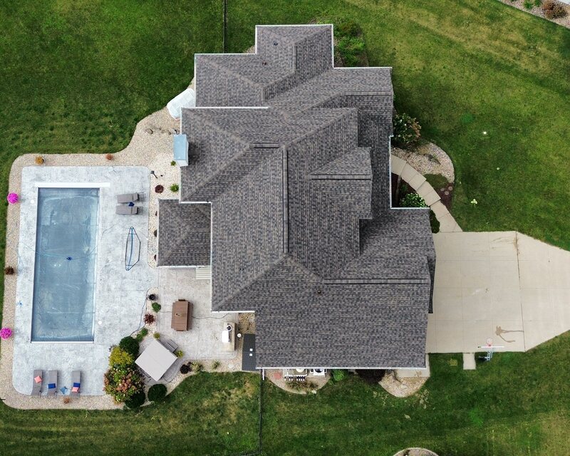 Top-down drone aerial of a completed roof replacement on an Oregon WI home, new grey architectural shingles, with a backyard pool and patio
