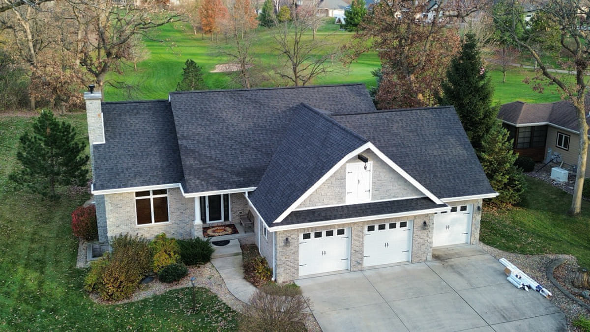 Same stone-faced home after roof replacement with new dark architectural asphalt shingles