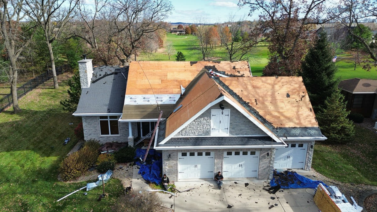 Stone-faced home with roof torn off and wood decking exposed, mid-roof-replacement aerial view