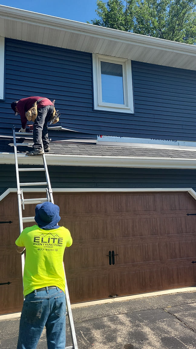 Elite crew installing navy blue lap siding over house wrap from a ladder on a northern Illinois home
