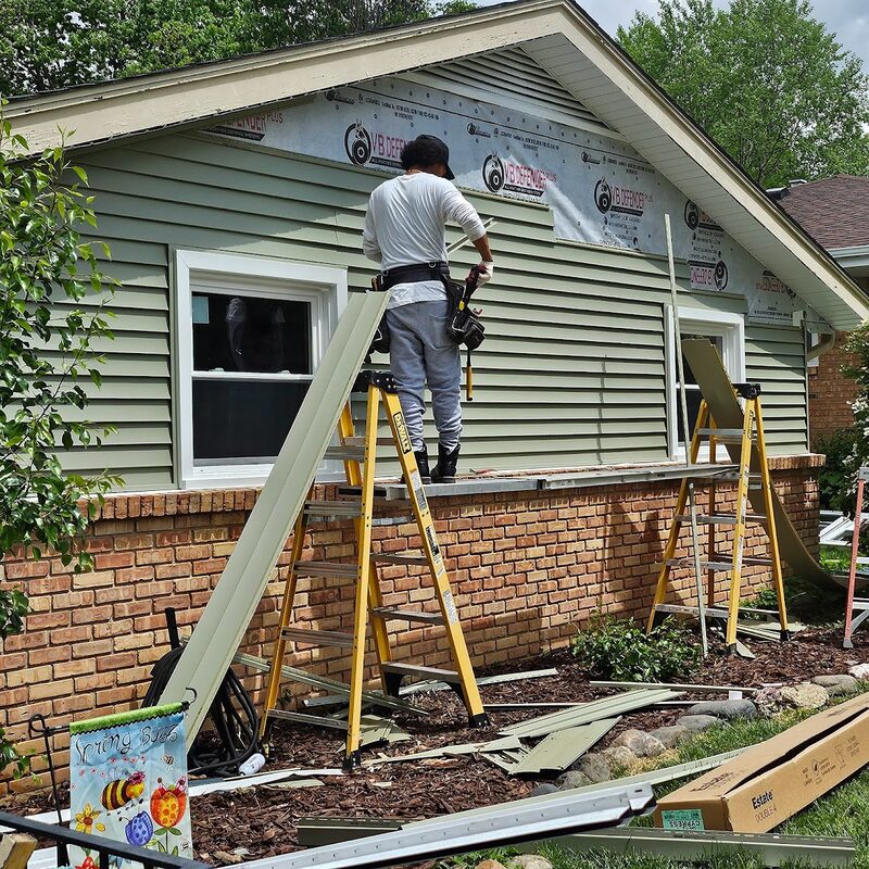 Crew installing green lap siding over exposed house wrap from a ladder during a siding replacement in northern Illinois