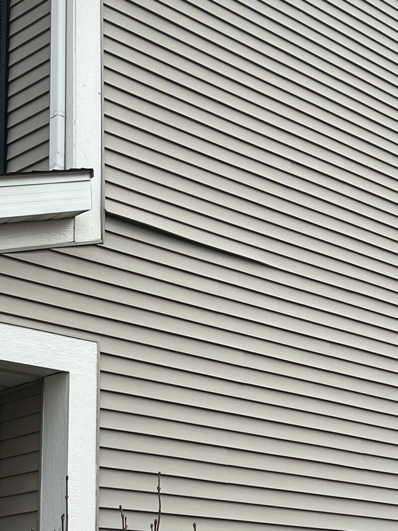 Lifted, buckled course of light grey vinyl siding high on a house wall needing siding repair in Loves Park IL