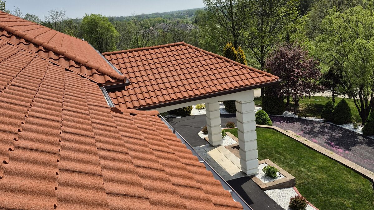 Finished stone-coated metal roof in a tile profile on a Brookfield WI home, terracotta steel panels that look like clay tile over a portico and landscaped yard