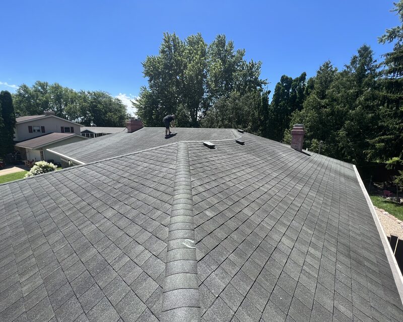 Elite roofer on the ridge during a roof inspection of a grey asphalt shingle roof in a Janesville WI neighborhood