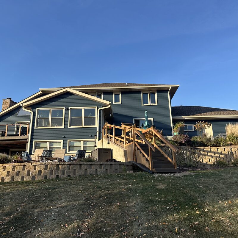 Finished blue-grey lap siding replacement on a large two-story Janesville WI home with a wood deck