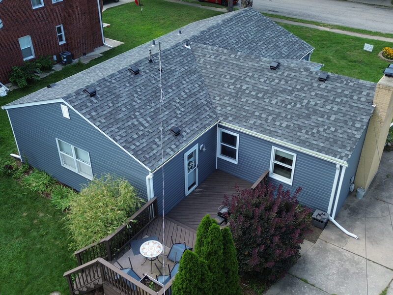 Aerial view of a completed asphalt shingle roof replacement on a 1952 single-story ranch in east Rockford IL with slate-blue siding