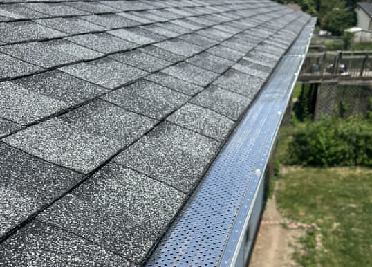 Black perforated aluminum leaf guard installed along the eave of a dark asphalt shingle roof