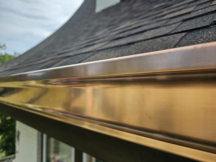 Polished copper K-style box gutter installed by Elite Contracting Group on a Decatur, Illinois home, photographed close along the eave with the asphalt shingle roof above