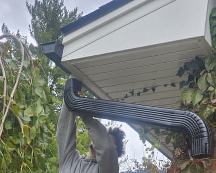 Elite installer fitting a new black downspout to seamless gutters at the eave during a gutter installation in Rockford IL
