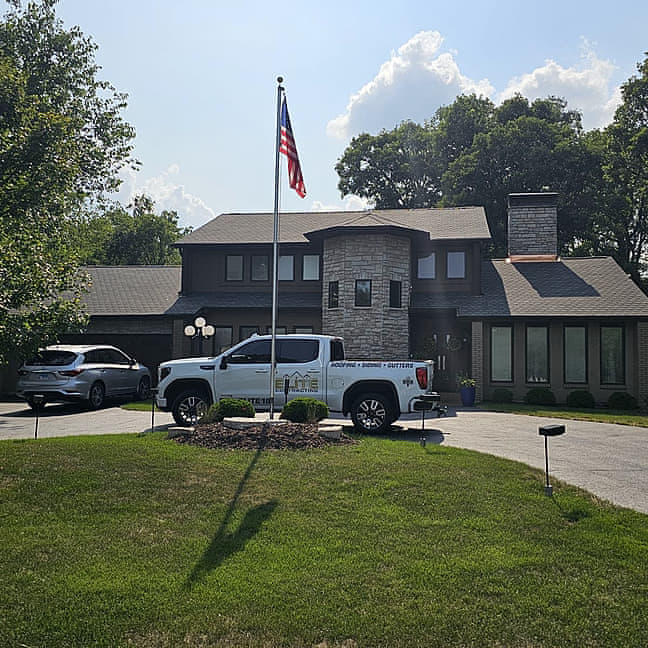 Modern two-story home in Orland Park, Illinois with a freshly installed dark asphalt shingle roof, branded Elite Contracting Group truck parked in the circle drive and an American flag flying